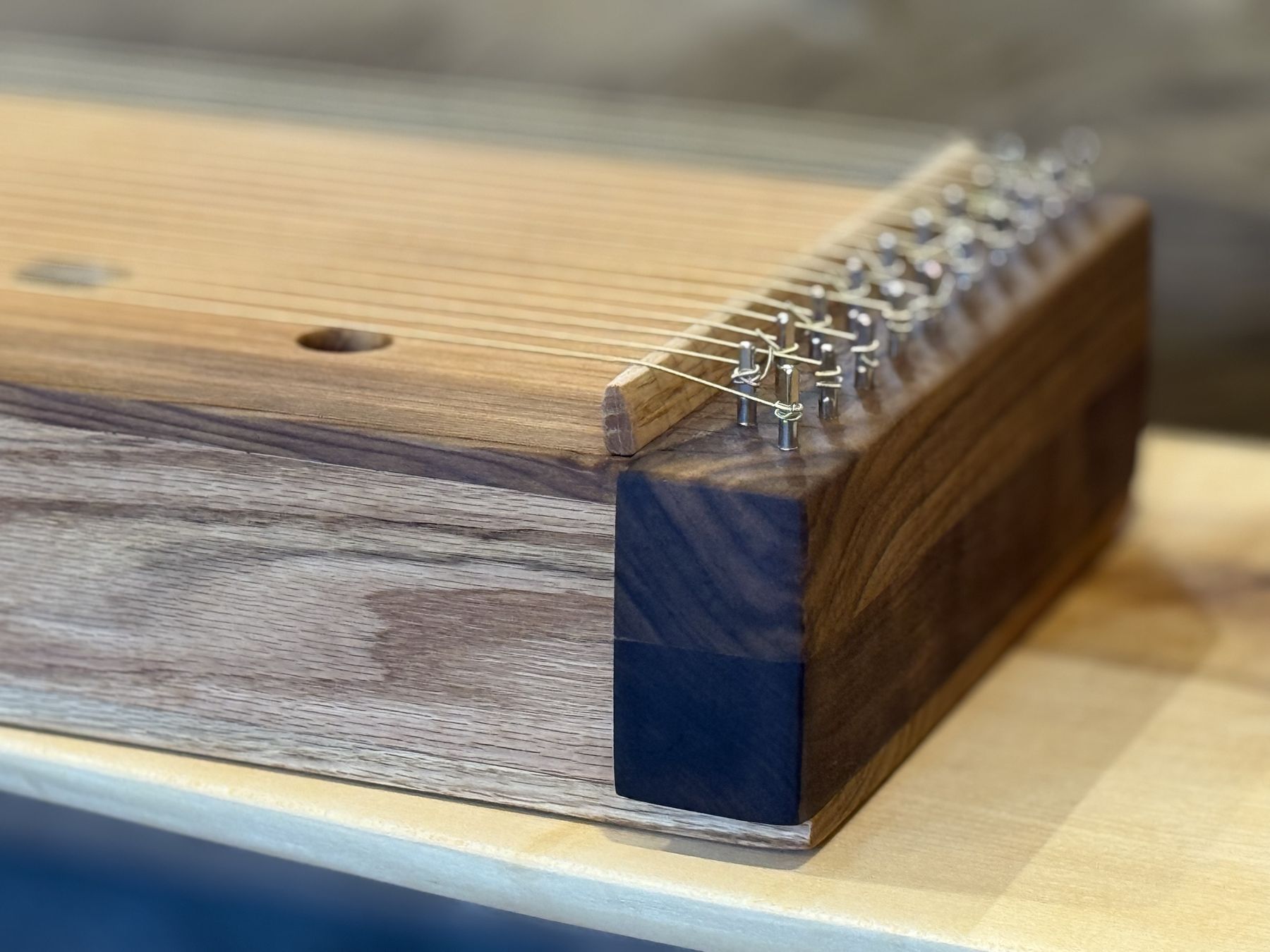Close view of steel tuning pins set in a walnut end block, with strings wound around each pin and crossing an oak bridge.